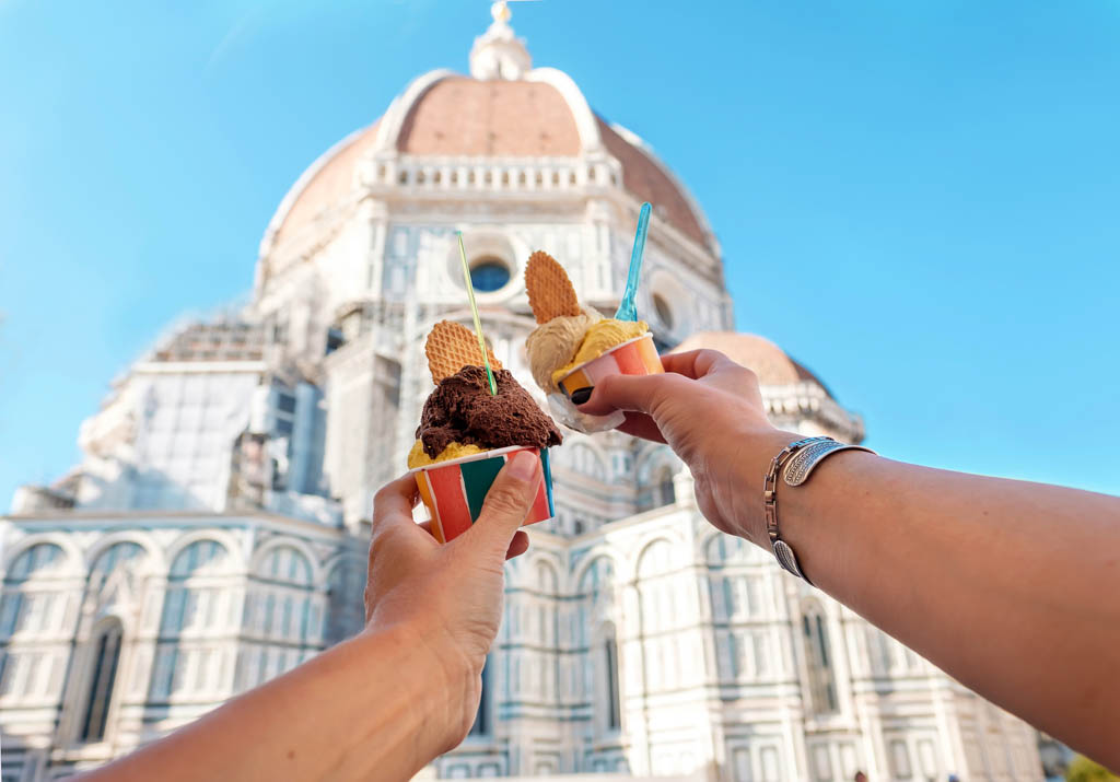 Women's hands with ice cream Gelato on the background of the city sight Cathedral of Santa Maria del Fiore in the historical center of Florence, Italy, Europe, a famous tourist place