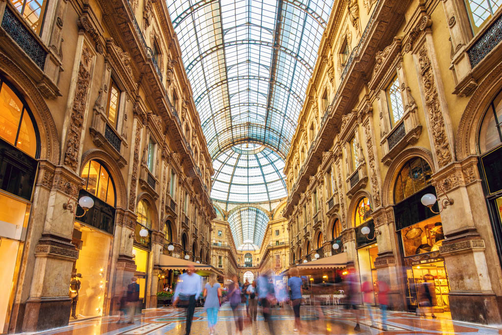 Shot of the famous Galleria Vittorio Emanuele II in Milano, Italy, the famous luxury shopping mall, showing the spectacular view of an almost golden gate to luxury. Long exposure with motion blurred people walking along the shops and restaurants. Milan, Lombardy, Italy