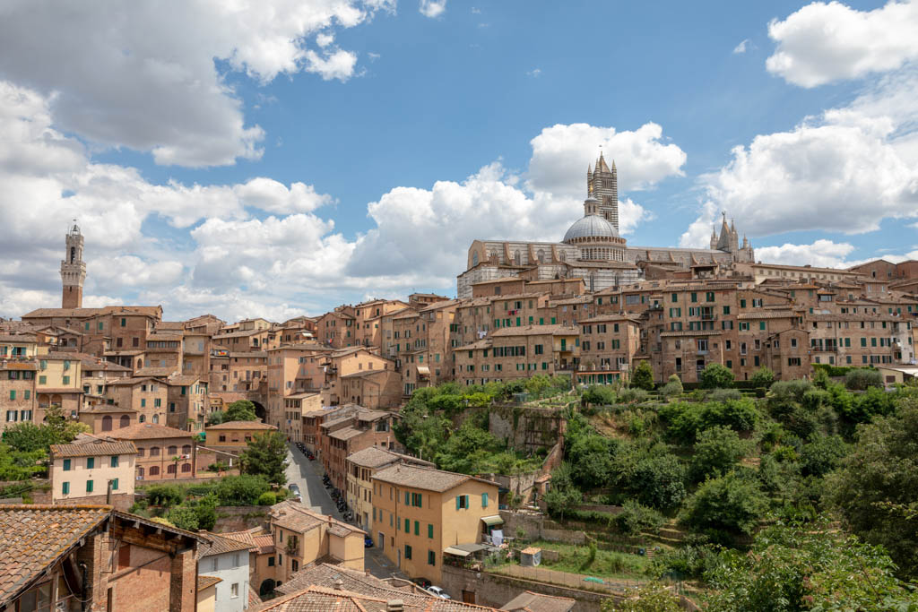 Panoramic view of Siena city with historic buildings and far away Siena Cathedral (Duomo di Siena). Summer sunny day and dramatic blue sky