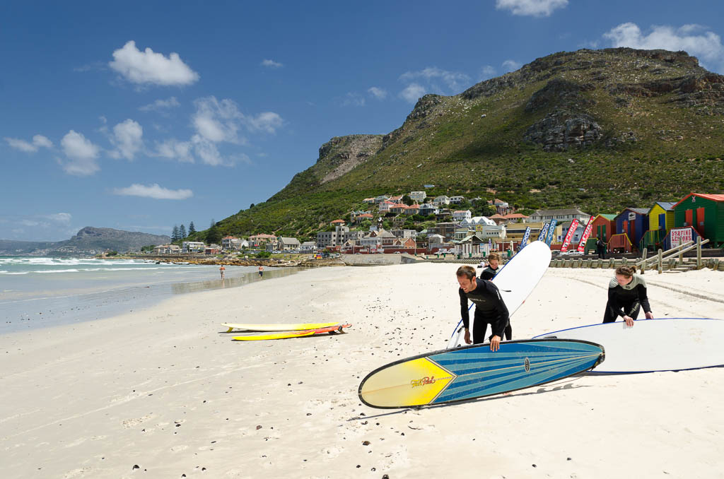 "Cape Town, South Africa - February 10, 2012: Three surfers are getting ready for a surf lesson in Muizenberg, near Cape Town in South Africa. Male surfer is more experienced and two female surfers will get some instructions from him before going into water. Muizenberg is one of the suburbs of Cape Town and it's famous with its colorful beach cottages. Another famous thing abouth Muizenberg is its surf schools and almost constant wind which makes it an ideal place for surfing."