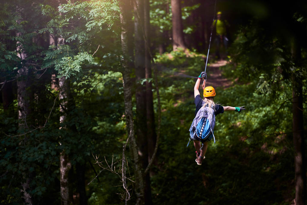 rear view of woman in the forest with her backpacker enjoying adventure on tyrolean traverse.