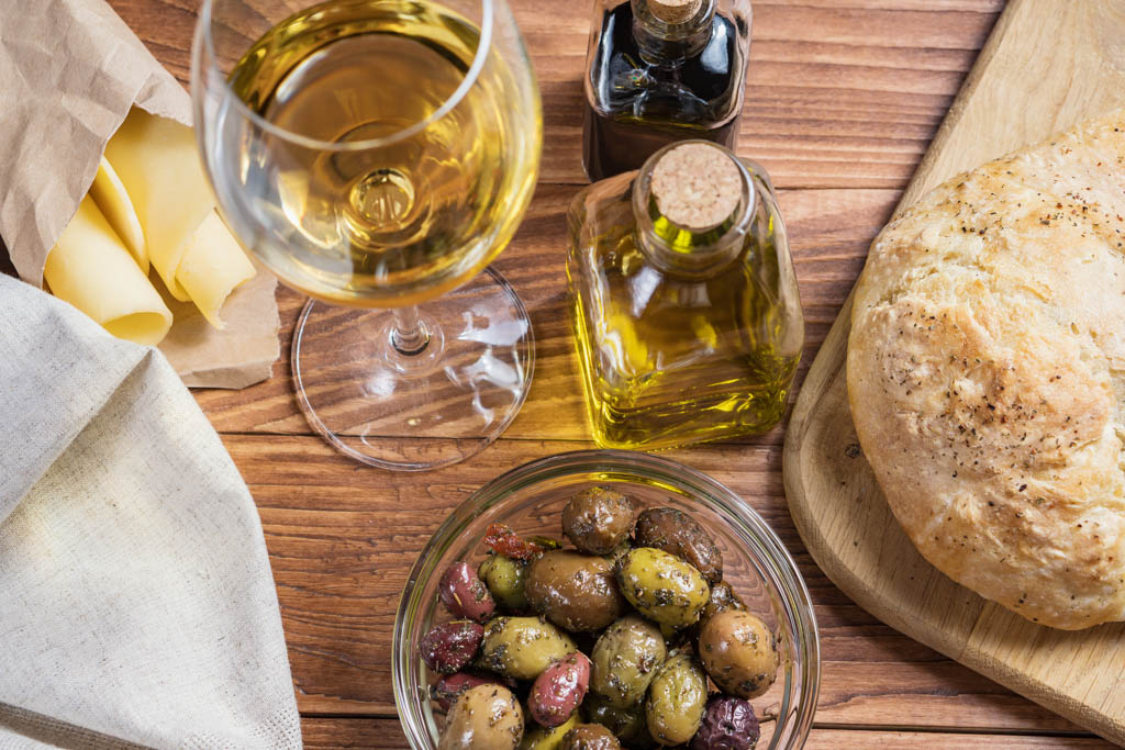 Bowl with different kind of olives, glass of wine, cheese and fresh bread ciabatta on the wooden table.