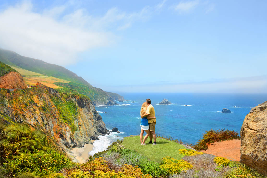 Loving embracing couple standing on top of mountain, looking at beautiful mountain landscape, on hiking trip. .Big Sur, California, USA