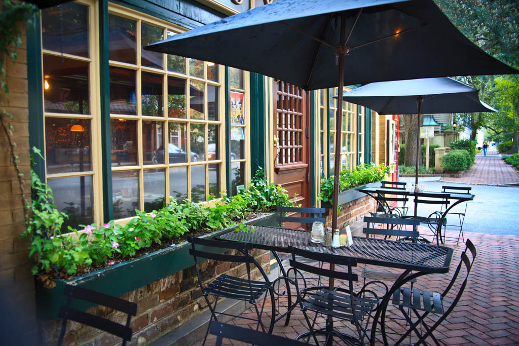 Cozy and picturesque street cafe (bistro) with window boxes, chairs, tables and umbrellas. Brick sidewalk, French windows and front door. City life; cafe society; small restaurant; Savannah, Georgia.