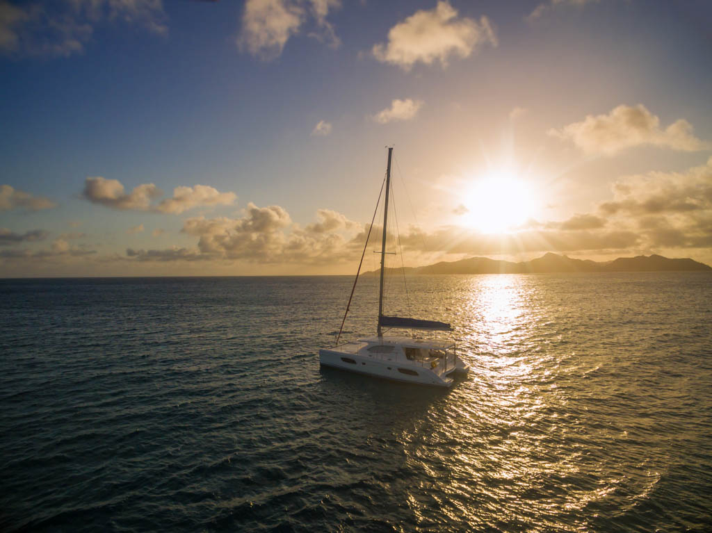 Aerial view of catamaran sailling in coastline with beautiful sunset. Tropical Seychelles island on background