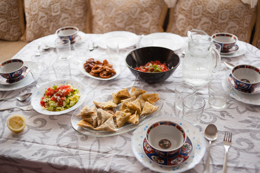 Interiors shot of a home dairy food table scene shot of a moroccan family environment with plates like salad, chebakia, dates and brewat and props like water, lemon, soup bowls, cutlery and glasses.