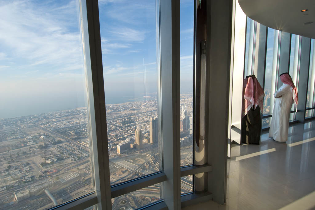 Two arab men in traditional dress looking out of the window over Dubai from the Burj Khalifa, the tallest building on earth