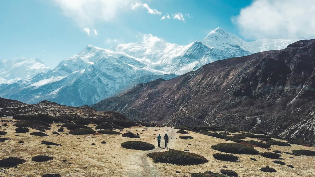 A couple trekking in the Manang Valley, Annapurna Circus Trek, Himalayas, Nepal, with the view on Annapurna Chain and Gangapurna. Dry and desolated landscape. High mountain peaks, covered with snow.