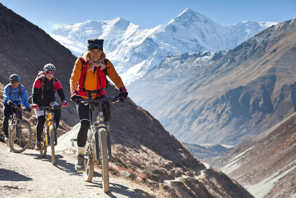 A female mountainbiker is leading a group on their ascend towards Thorong La (5.416 mt, 17.770 ft), the highest point on the Annapurna Circuit, Nepal. This trekking route is one of the most famous trails in the world. The bikers are above 3.500 mt (11.500 ft) altitude; the summits of the Annapurna range in the background are above 7.000 mt (23.000 ft).