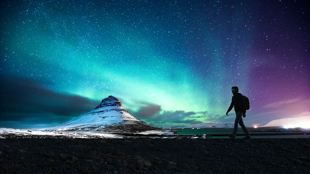 Solo traveler walking in front of an awesome Northern Lights in Mount Kirkjufell Iceland.