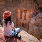 Asian woman traveler sitting on carpet viewpoint in Petra ancient city looking at the Treasury or Al-khazneh, famous travel destination of Jordan and one of seven wonders. UNESCO World Heritage site.