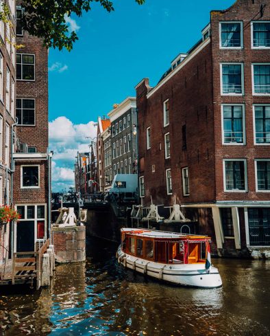Small Tourist boat floating picturesque dutch channel passing traditional brick houses. Colorful cityscape in Amsterdam Netherlands, Europe. City trip concept.