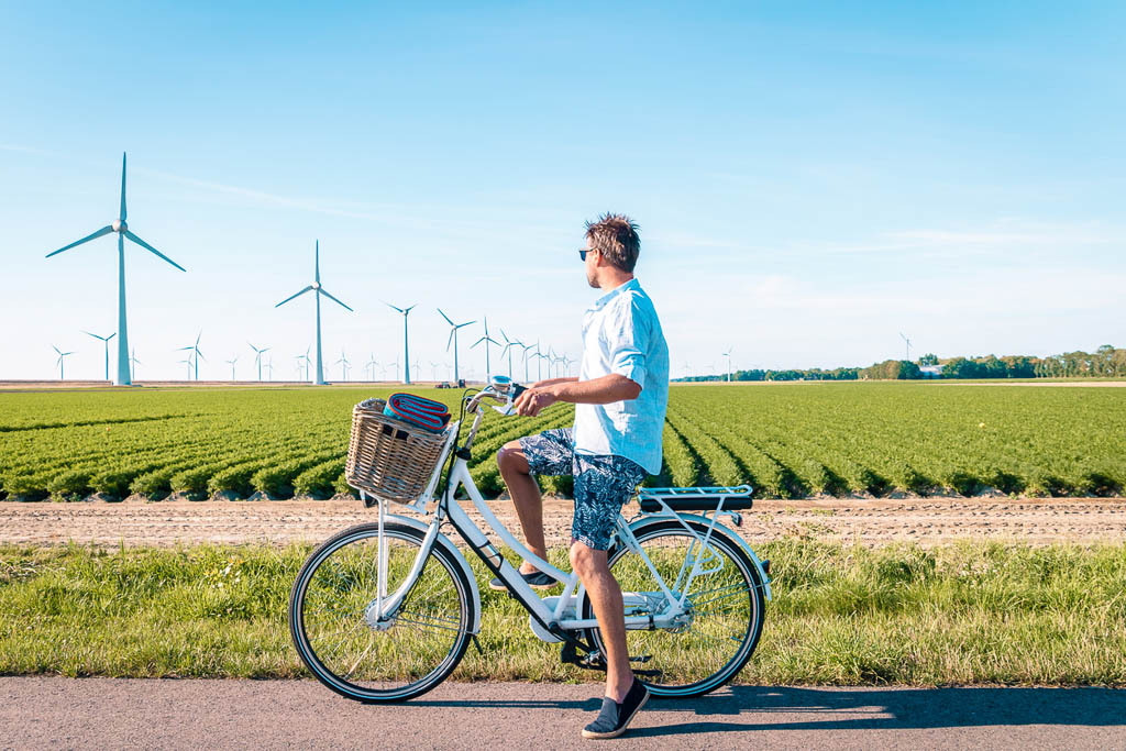 Dutch young man electric green bike bicycle by windmill farm , windmills isolated on a beautiful bright day Netherlands Flevoland Noordoostpolder