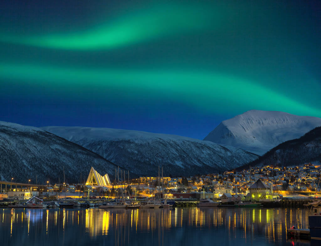 View at night on illuminated Tromso city with cathedral and majestic aurora borealis