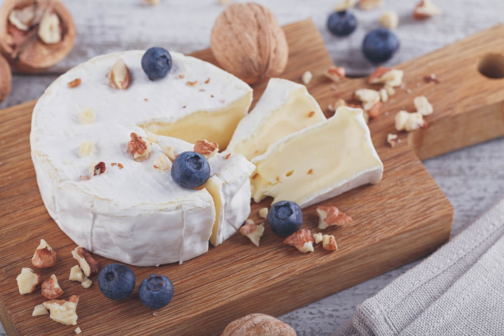 Soft french cheese of camembert served with chopped walnuts and blueberries on wooden plate.