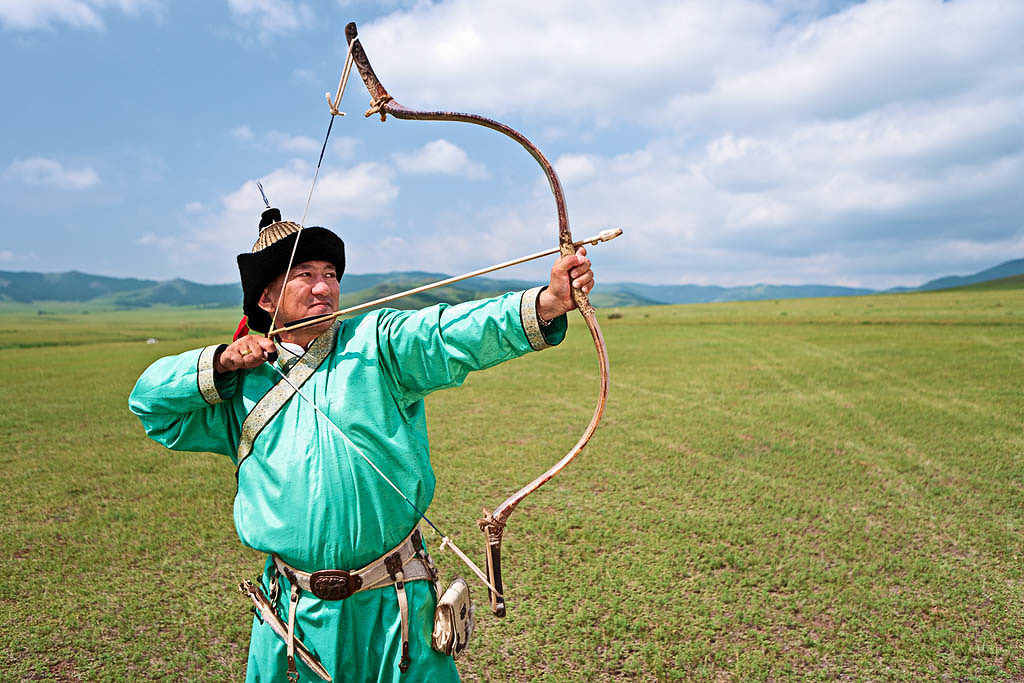 "Mongolian archer standing on the grass, the blue sky on the background."