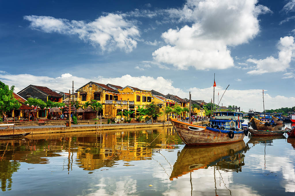 Wooden boats on the Thu Bon River in Hoi An Ancient Town (Hoian), Vietnam. Yellow old houses on waterfront reflected in river. Hoi An is a popular tourist destination of Asia.