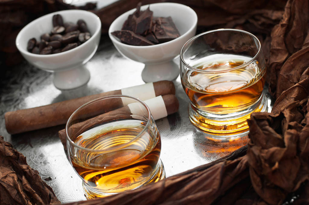 Elegant tray with two glasses of rum, cuban cigars, chocolate and coffee beans. The tray is adorned with tobacco leaves.